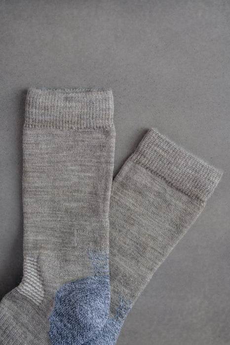 Pair of beige merino wool socks with blue accents on a grey background