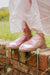 Warm Pink Sheepskin Slippers Womens 
worn by woman stood on a re brick wall wearing a floaty pink skirt 