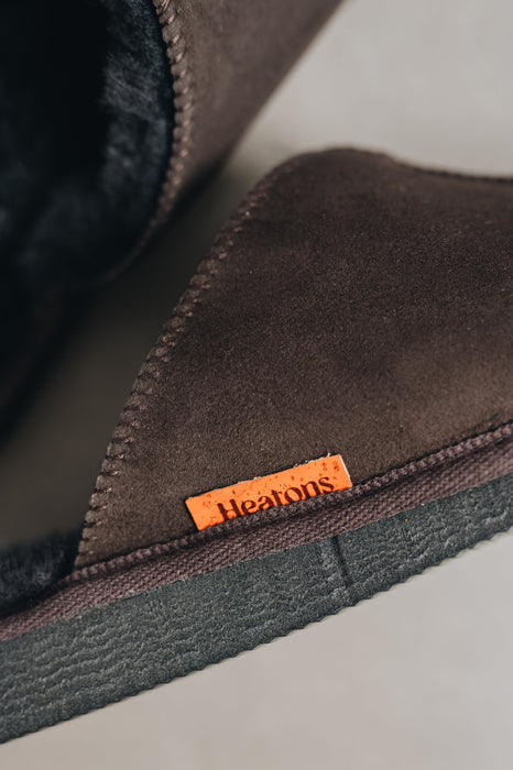 Close up of a pair of dark brown merino sheepskin men's mule slippers with an orange cork Heaton's label