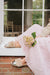 Silver Veronica Sheepskin Slippers with a turn back cuff for women, worn by a young woman sat on a window ledge. She's wearing a pink tulle skirt and holding a bunch of pink Hydrangeas.