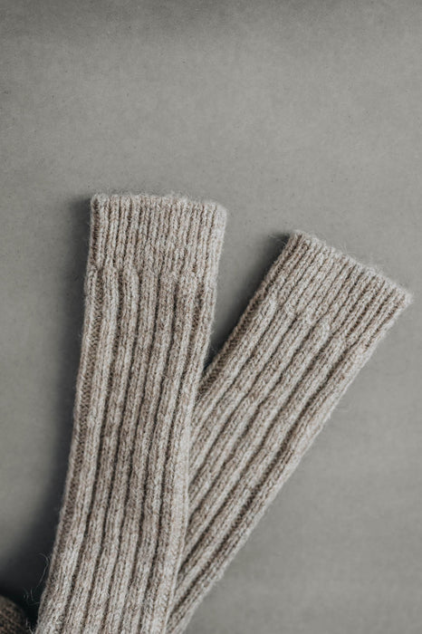 Ribbed beige natural merino wool sock on a light grey background - detail of ribbed sock neck