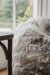 Close-up of a natural melange bean bag next to a wooden chair with a blurred background