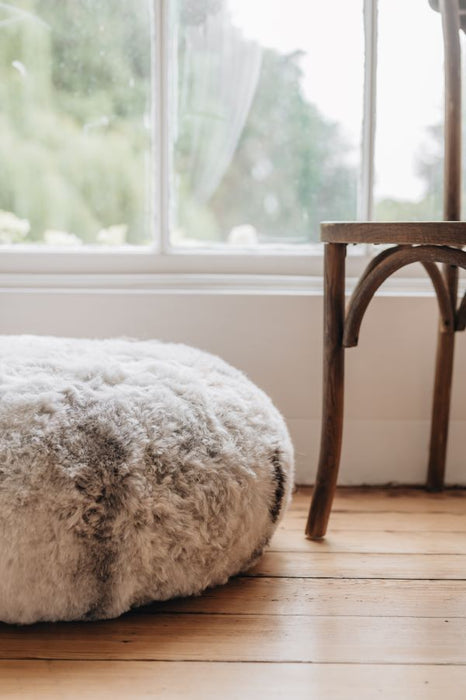 Close up melange shearling ottoman on a wooden floor with a blurred window in the background