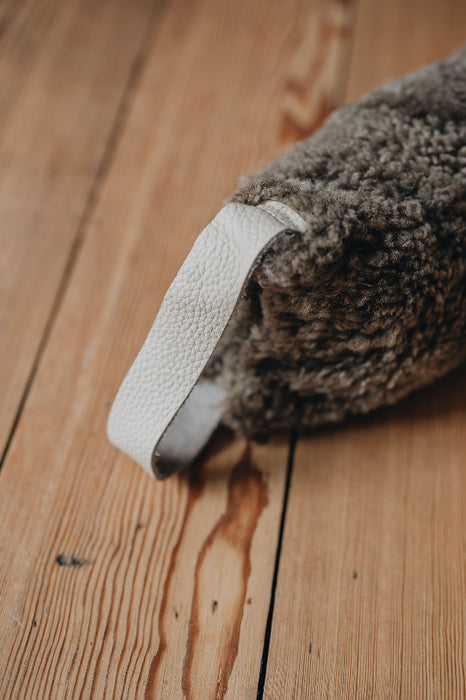 Brown sheepskin draught excluder with light handle on a wooden floor