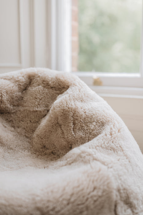 Close-up of an oatmeal sheepskin beanbag with a blurred window background.