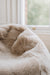 Close-up of an oatmeal sheepskin beanbag with a blurred window background.
