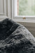Close-up of a black smoke coloured sheepskin beanbag with a blurred window background.