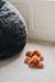 Pair of rust coloured sheepskin slippers on a light  carpet next to a large dark sheepskin bean bag chair.