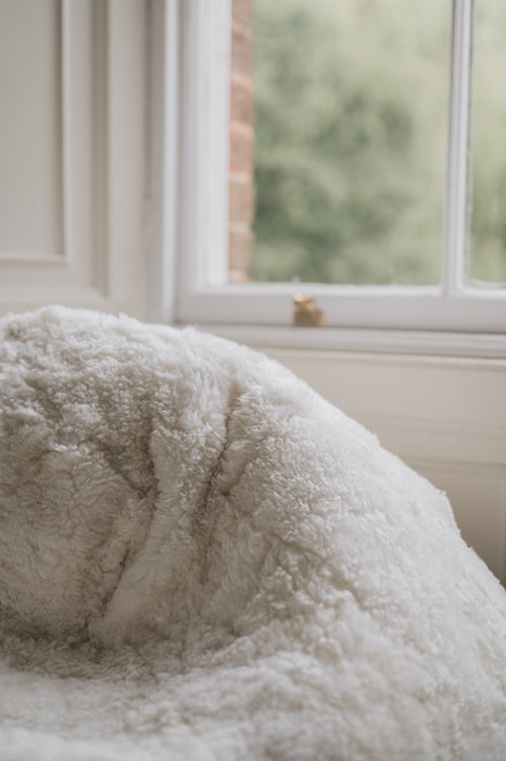 Close-up of a white sheepskin beanbag with a blurred window background.