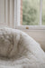 Close-up of a white sheepskin beanbag with a blurred window background.