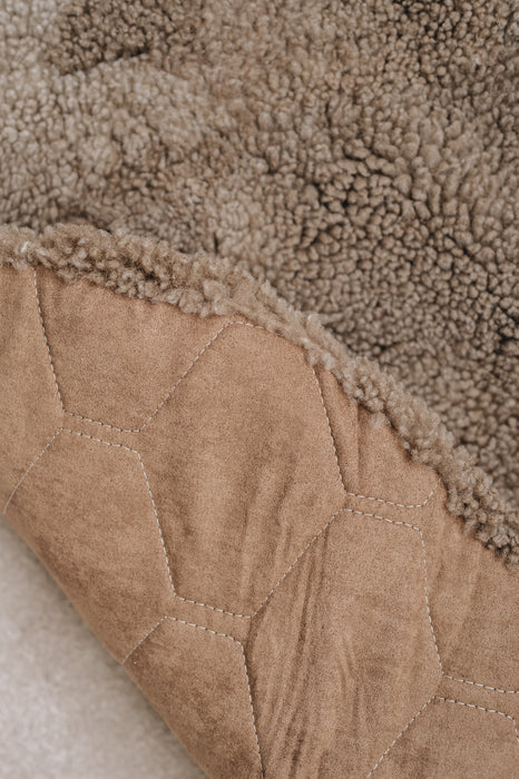 Close-up of a textured brown fabric surface with a geometric pattern that is the underside backing of a wheat brown sheepskin rug