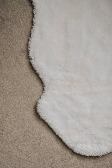 Close-up of a whitel sheepskin rug on a light coloured carpet