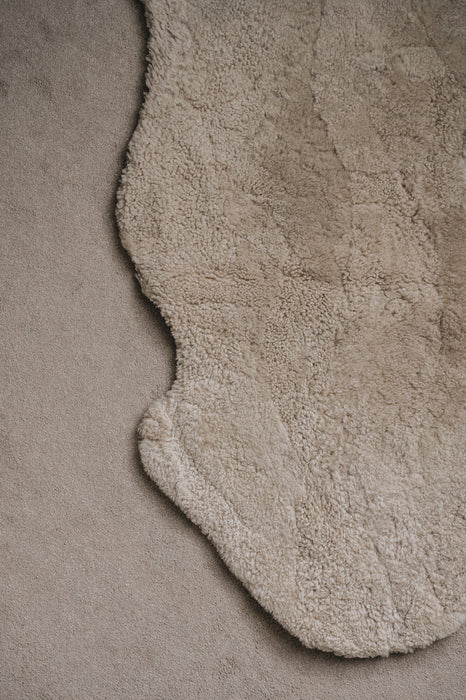 Close-up of an oatmeal sheepskin rug on a similar coloured carpet