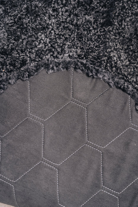Close-up of a textured dark fabric with a honeycomb pattern on the back / underside of a grey / black sheepskin rug