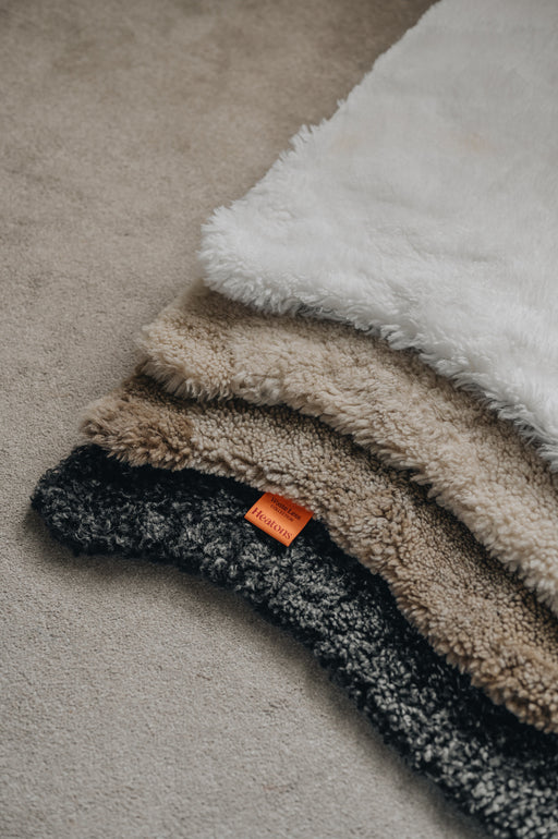 Stack of sheepskin rugs in various colours on a neutral carpet