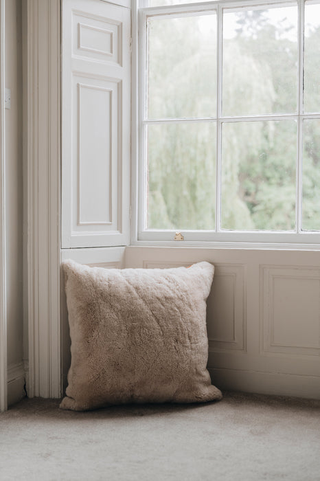 Oatmeal sheepskin floor cushion on a floor in a room with a large window