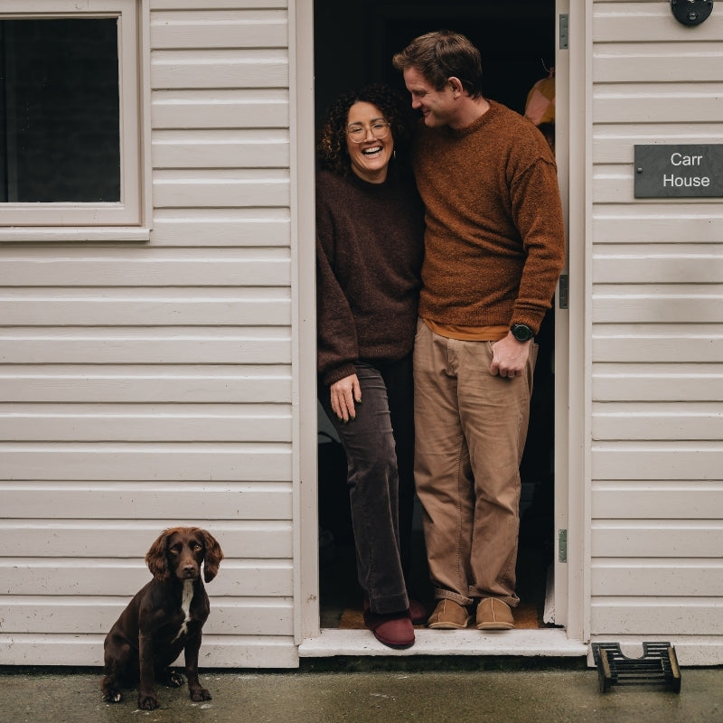 Two people wearing slippers standing in a doorway with a dog sitting outside.