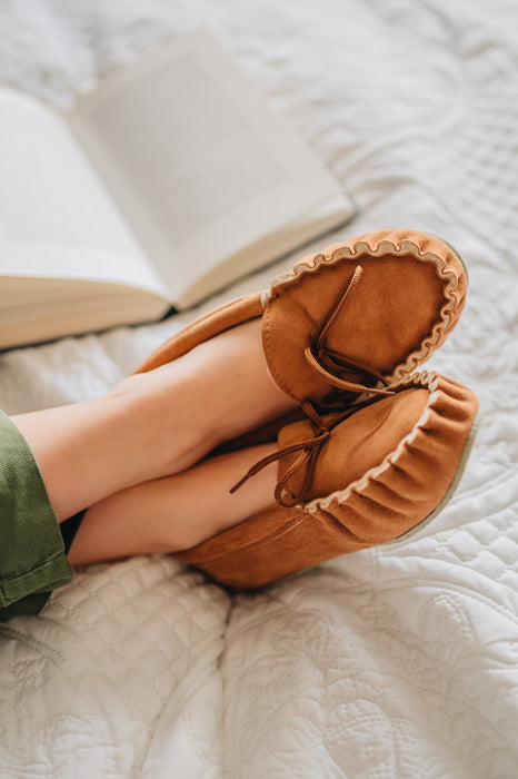 Ava Women's Real Sheepskin Moccasins worn by model with feet up on a bed reading a book 
