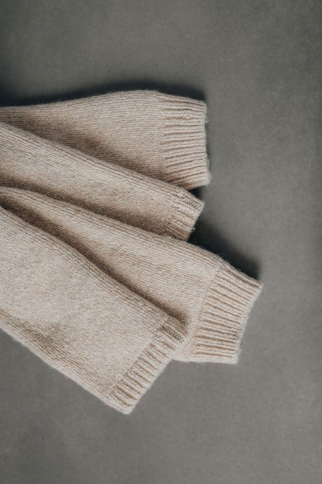 Folded beige wool legwarmers on a gray background