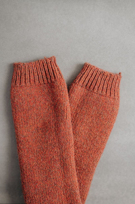 Pair of rust knitted woolen leg warmers on a gray background