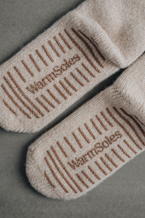 Beige wool slippers socks with 'WarmSoles' branding on a gray background