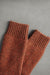 Pair of rust coloured knitted wool bed socks on a gray background
