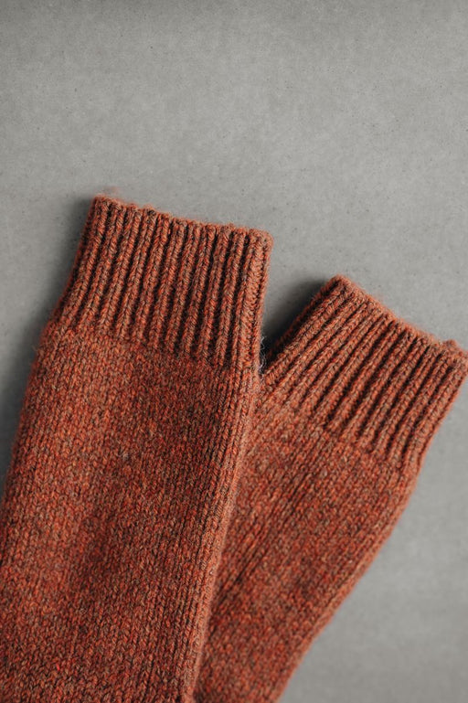 Pair of rust coloured knitted wool bed socks on a gray background