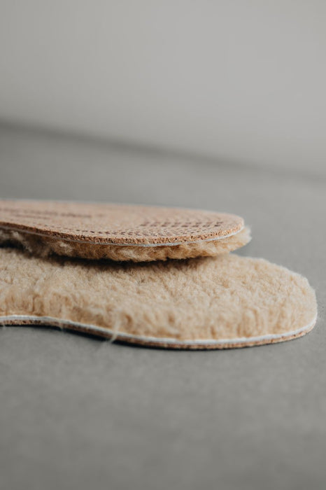 Pair of beige shoe sheepskin inserts on a gray background