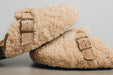 Side view of a vanilla coloured curly sheepskin mule, showing of it's adjustable sheepskin strap and quality buckle