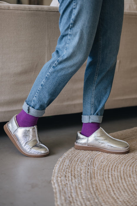 Cadi Silver Sheepskin Slippers on Concrete Surface worn by leady in jeans and purple socks