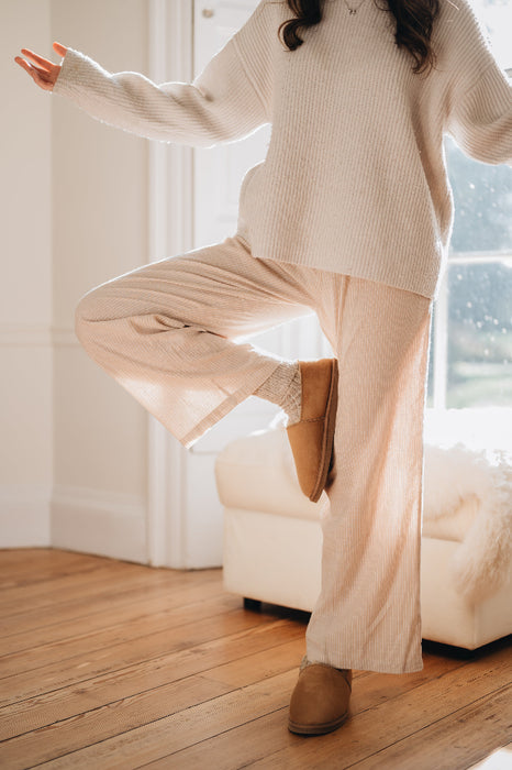 Young woman wearing the Tilly sheepskin slipper whilst balancing on one leg calmly , stood in a floor to ceiling window.