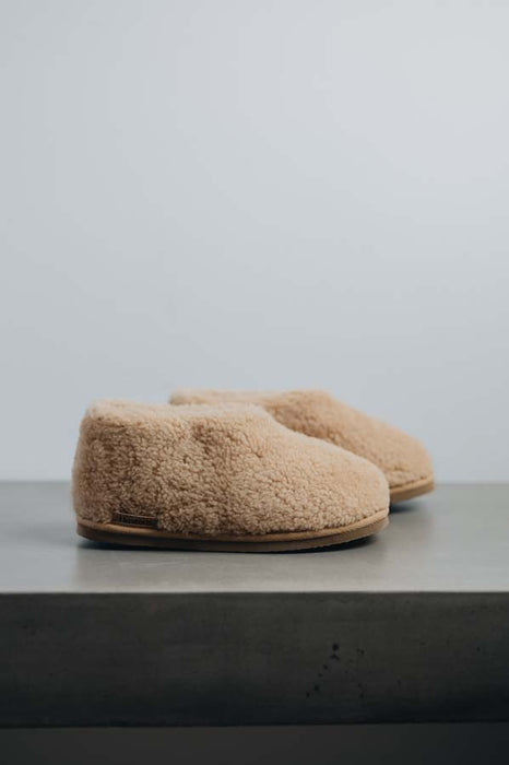 Side view of a camel coloured curly merino sheepskin boot slipper.