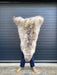 sheepskin rug being held up to show natural markings, cream with light brown dappled markings