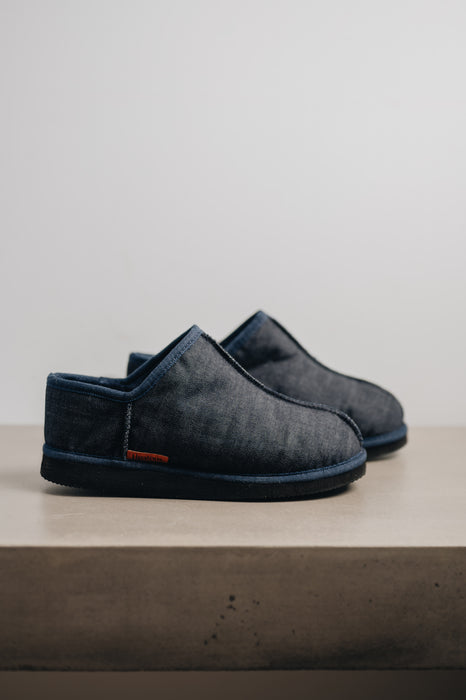 Mens Sheepskin Slipper with Denim Exterior for durability. Profile view on a stone bench.