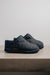 Mens Sheepskin Slipper with Denim Exterior for durability. Profile view on a stone bench.