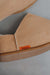 Close-up of a tan pair of Cadi sheepskin slippers with a small orange Heaton's brand label, resting on a neutral grey surface.