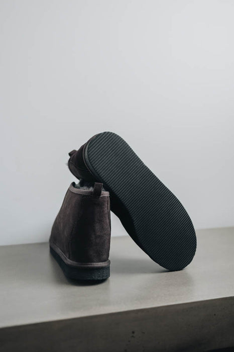 Dark brown Erin women's sheepskin slippers with black soles on a light gray surface and white background