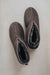Pair of dark brown sheepskin slippers with wool lining on a light grey background. Birds eye view.