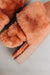 Close-up of a pair of fluffy rust coloured sheepskin slippers with an elasticated band and an orange cork Heatons brand label on a light background