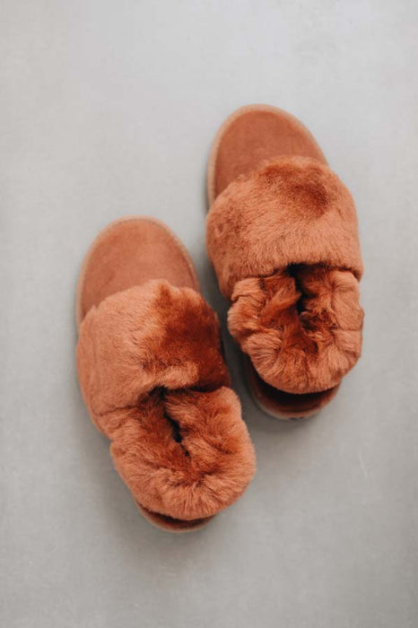 Pair of rust coloured sheepskin slippers with fuzzy texture on a light grey background