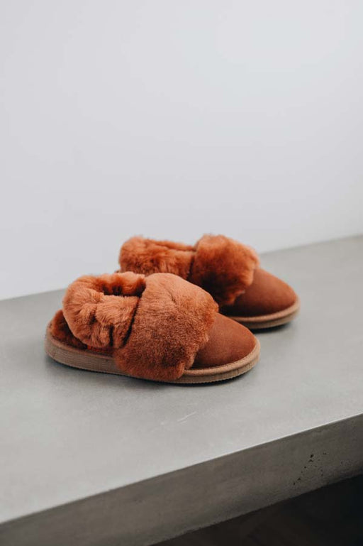 Pair of rust sheepskin slippers with fuzzy texture on a light grey stone surface.