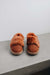 Front view of a pair of rust coloured sheepskin slippers on a light grey surface with a white background