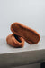 Suede underside of a pair of rust curly sheepskin slippers on a light grey stone bench with a neutral background