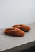 Pair of rust coloured curly sheepskin slippers on a concrete surface with a light grey background