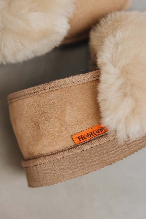 Close-up of a tan suede slipper with fluffy cream shearling lining and an orange 'Heatons' brand tag.