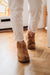 Men's boot slippers with sheepskin with hard sole. Named Huw and rafted from Spanish Merino. Worn by man walking away from a stained glass door on an oak floor.