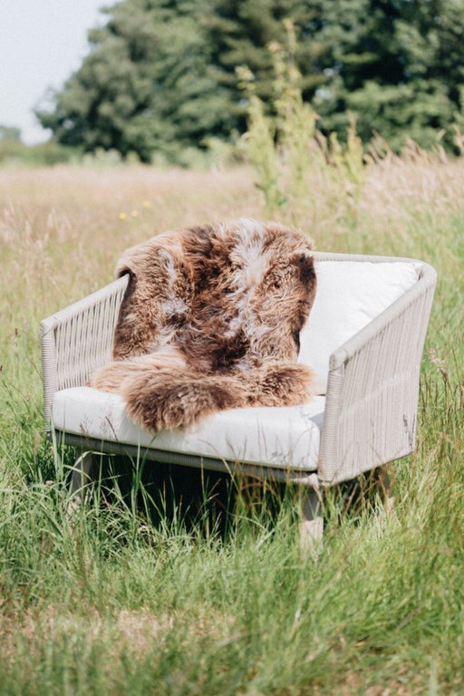 Dark Toned Rare Breed British Sheepskin Rug draped across a Garden chair in an English Meadow.