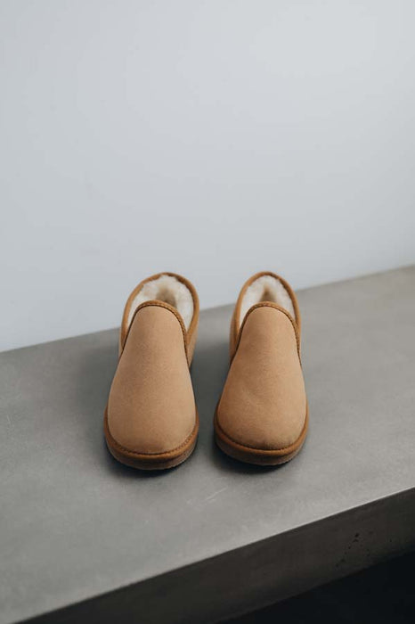 Pair of tan sheepskin slippers on a grey stone surface with a white background