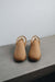 Pair of tan sheepskin slippers on a grey stone surface with a white background