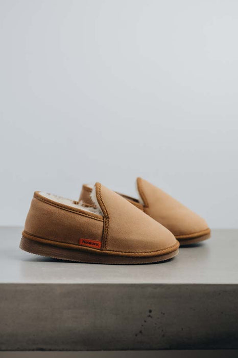 Profile view of a pair of tan sheepskin slippers on a grey stone surface 